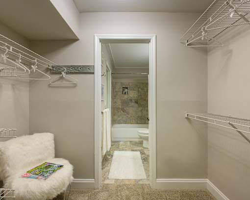 A white chair with a fluffy seat sits in a hallway with a white doorway leading to a bathroom.