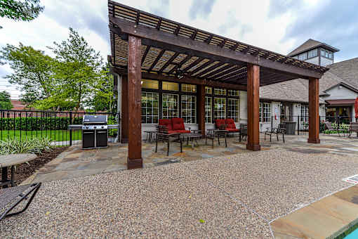 A wooden pergola with red chairs and a stone patio.