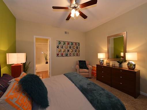 A bedroom with a bed, a chair, a dresser, and a ceiling fan.