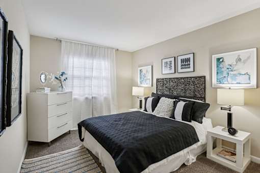 A bedroom with a white bed and a white nightstand with a lamp.