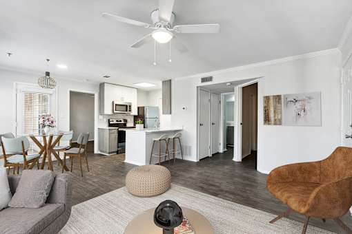 A modern living room with a grey sofa, wooden chairs, and a white ceiling fan.