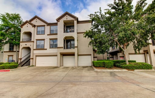 front view of an apartment building with garages and trees at Stone Creek at Old Farm Apartments, Houston