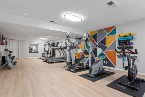 a gym with cardio equipment and a colorful wall