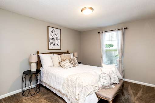 A bedroom with a bed, a bench, and a lamp.