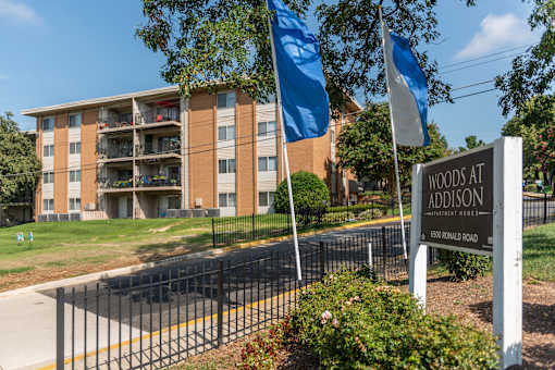 A sign for Woods at Addison stands in front of a building.