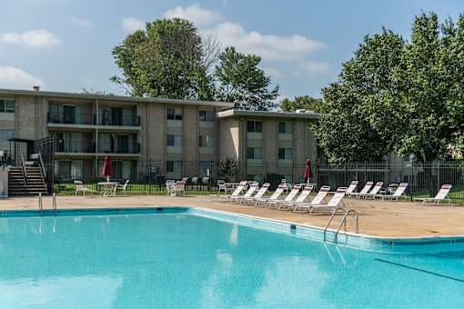 A swimming pool in front of a building with lounge chairs around it.