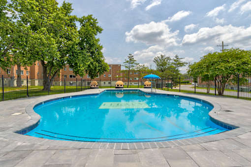 A round blue swimming pool surrounded by a black fence and trees.