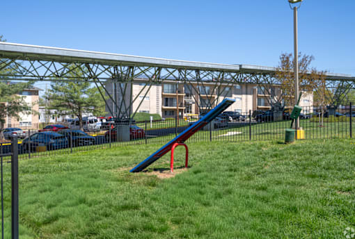 A playground with a blue and red slide in the foreground and a metal structure in the background.