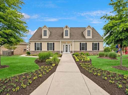 A house with a grey roof and a white door is surrounded by a garden with yellow flowers.