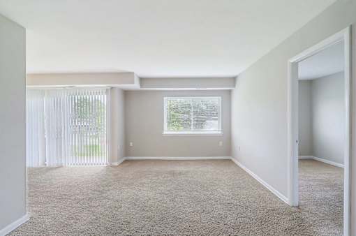 A room with a carpeted floor and a window with blinds.