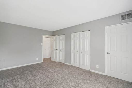 A room with grey walls and carpeted floor with three white doors.