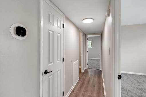 A hallway with a white door and a white wall with a round black device on it.
