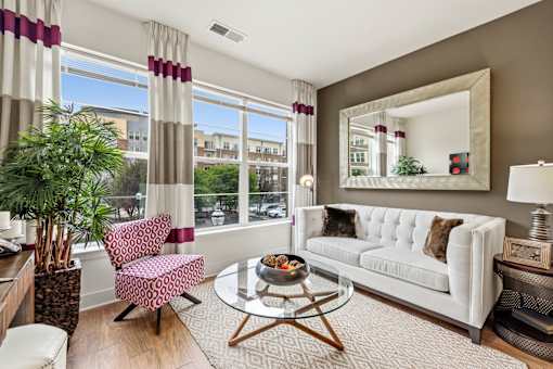 A living room with a white couch, a coffee table, and a large window with curtains.