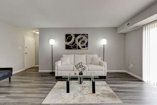 A modern living room with a white couch and a large abstract painting on the wall.