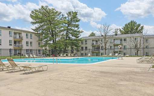 A pool surrounded by chairs and trees in front of apartment buildings.