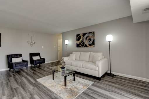 A living room with a white couch, a black chair, and a glass coffee table.