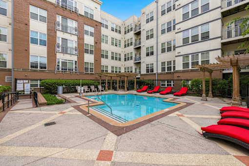 A swimming pool surrounded by red lounge chairs and apartment buildings.