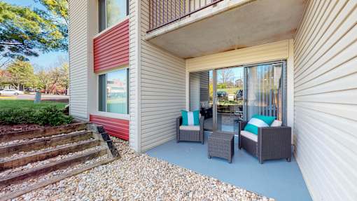 A patio with a couch, chairs, and a table is on the front porch of a house.