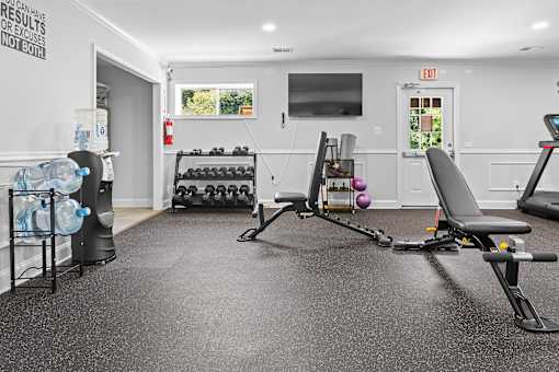 A gym room with a row of dumbbells and a bench.