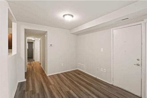 a living room with white walls and wood flooring and a door to a hallway