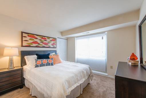 A bedroom with a bed, nightstand, lamp, and a painting on the wall.