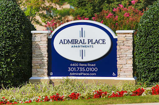 A sign for Admiral Place Apartments is displayed in front of some flowers.
