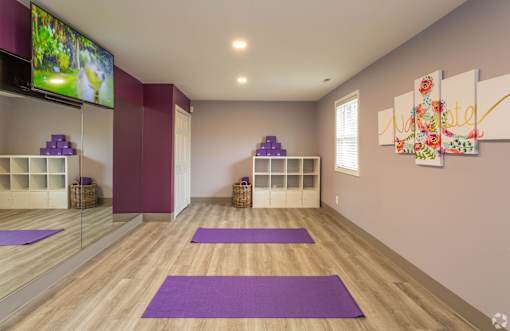 A yoga studio with purple mats and a flat screen TV mounted on the wall.