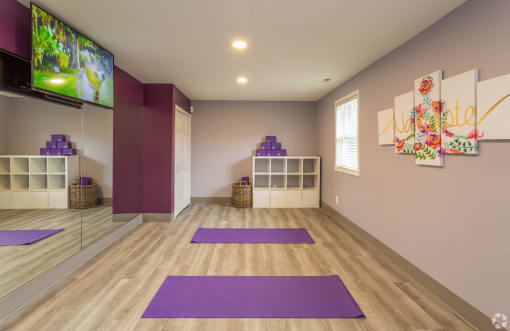 a yoga room with purple yoga mats and a tv