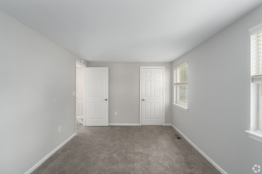 an empty bedroom with two doors and a carpeted floor
