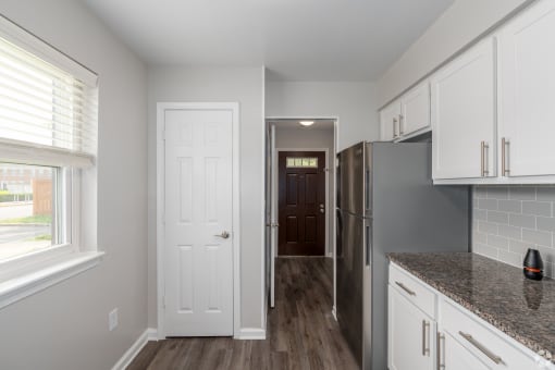 a kitchen with white cabinets and a door to a hallway with a refrigerator
