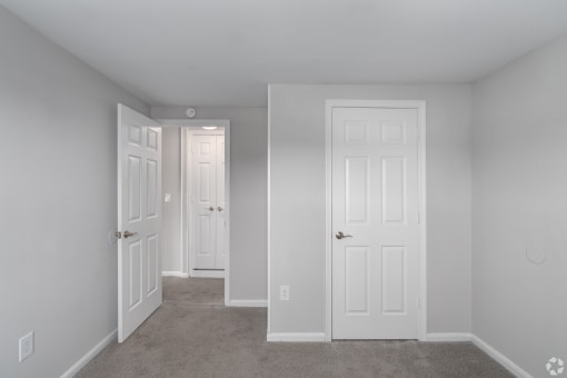 an empty bedroom with two doors and a carpeted floor