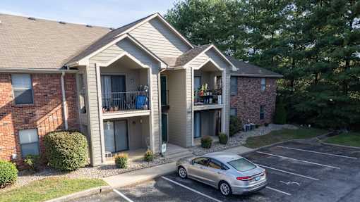 A silver car is parked in a parking lot in front of a two-story apartment building.