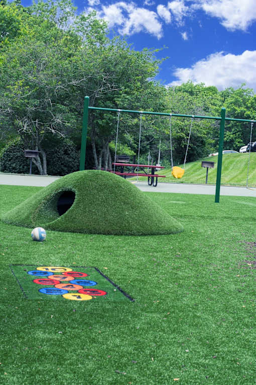 A playground with a green hill and a swing set.