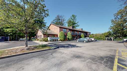 the front of a brick building with a parking lot and trees