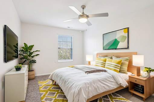 A bedroom with a bed, a ceiling fan, and a painting on the wall.