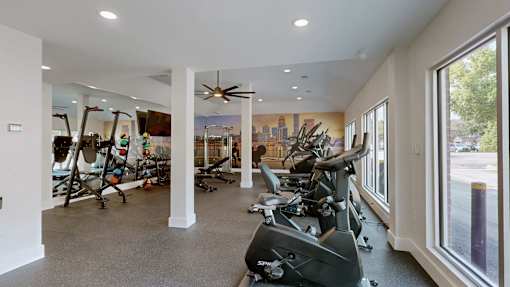 A gym with a row of stationary bikes and a fan.