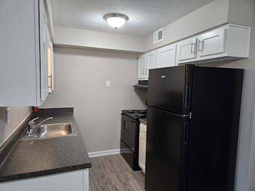 an empty kitchen with a black refrigerator and a sink