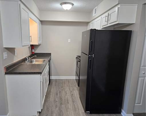 A black refrigerator sits in a kitchen with white cabinets.