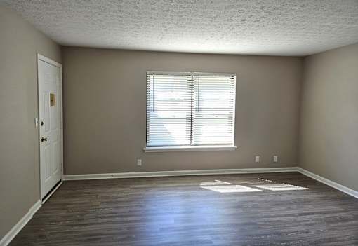 A room with a wooden floor and a window with blinds.