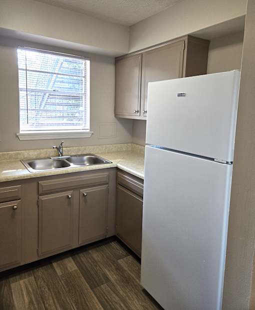 A white refrigerator stands in a kitchen with wooden floors and beige cabinets.