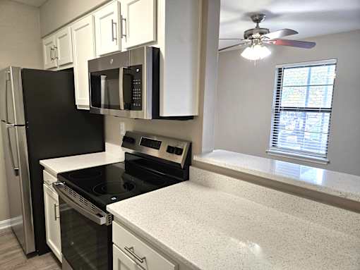 A kitchen with a black refrigerator, white cabinets, a black microwave, a black stove, and a white countertop.