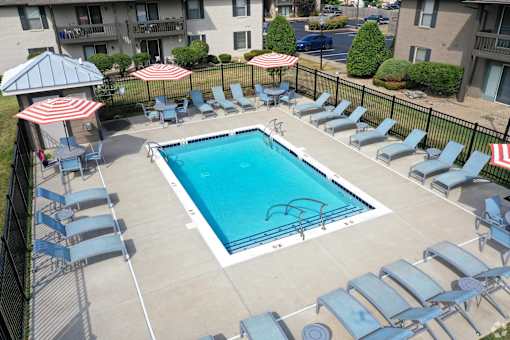 an aerial view of a pool with chairs and umbrellas and an apartment building