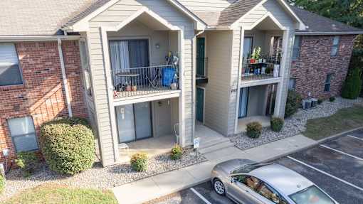 A silver car is parked in front of a two-story apartment building.