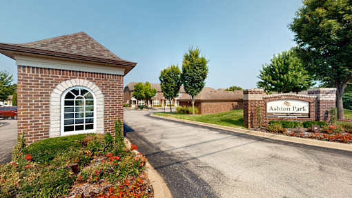 A small building with a sign that says "Ashton Park" in front of a brick wall.