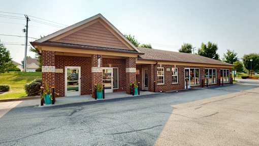 A small brick building with a brown roof and a parking lot in front.