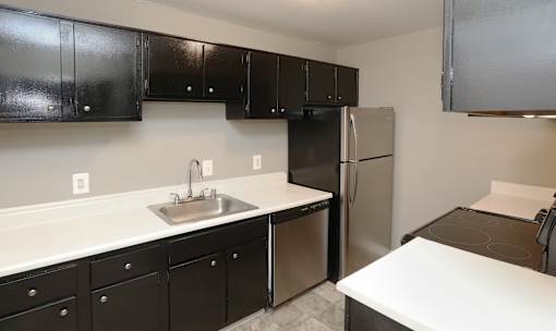 A kitchen with black cabinets and a stainless steel refrigerator.