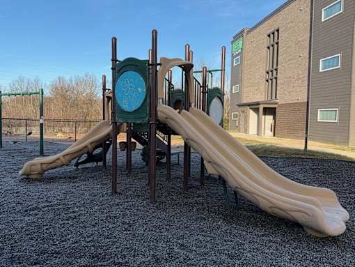 A playground with a slide and a green sign with a blue circle and a white symbol in the middle.