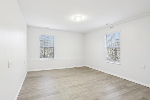 A room with a wooden floor and two windows with blinds.