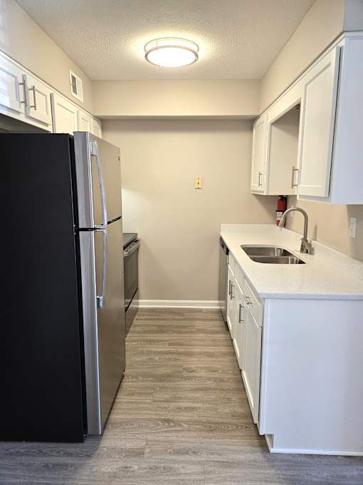 A black refrigerator is in a kitchen with white cabinets.