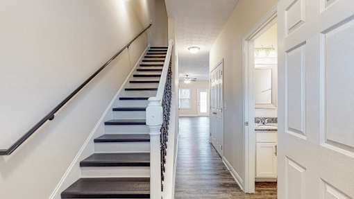 A long hallway with a staircase on the left and a kitchen area on the right.